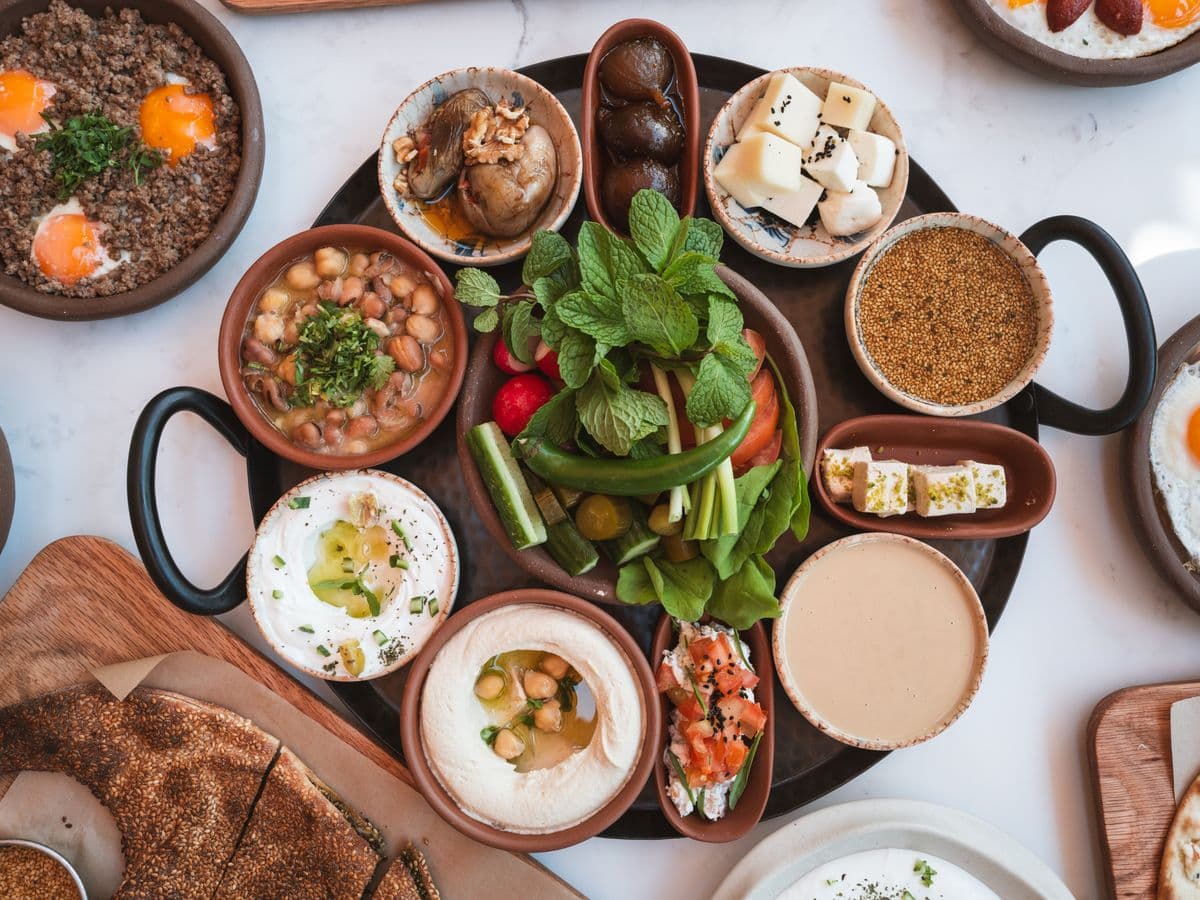 Grande table libanaise garnie de houmous, labneh, foul, fromages, menthe fraîche et pain