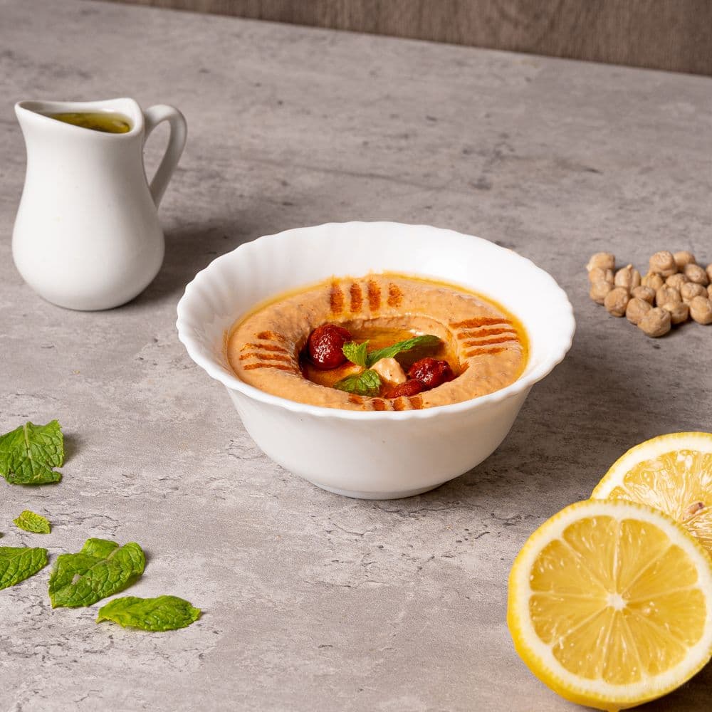Bol de houmous crémeux nappé d'huile d'olive, avec pois chiches, menthe et citron