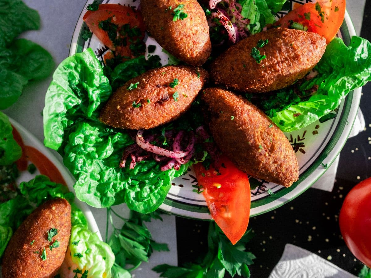 Kibbeh dorés servis sur un lit de laitue avec tomates et oignons au sumac