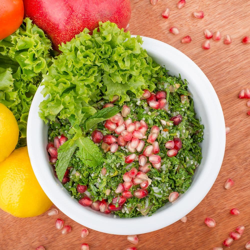 Taboulé au persil plat, boulgour et grains de grenade, entouré de citrons et de salade